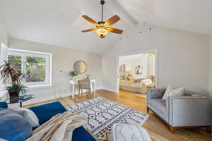 Living area featuring lofted ceiling with beams, light wood-style flooring, a ceiling fan, and baseboards