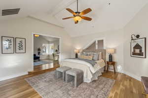 Bedroom with visible vents, wood finished floors, baseboards, ceiling fan, and vaulted ceiling with beams