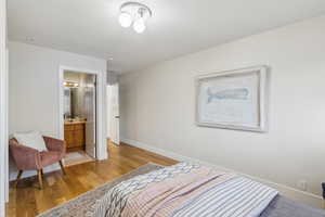 Bedroom featuring ensuite bath, light wood-style flooring, baseboards, and a sink