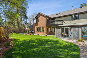 Back of house featuring fence, brick siding, a sunroom, and a lawn