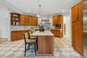 Kitchen with light floors, a breakfast bar, light countertops, appliances with stainless steel finishes, and wall chimney range hood