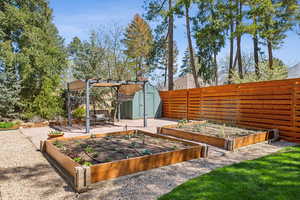 View of yard featuring fence private yard, a pergola, an outbuilding, a vegetable garden, and a storage unit