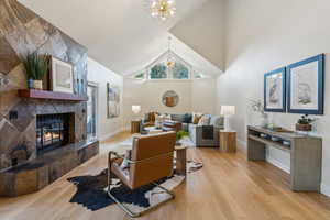 Living room featuring wood finished floors, baseboards, high vaulted ceiling, an inviting chandelier, and a tile fireplace