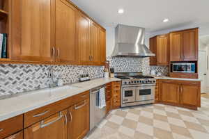 Kitchen with a sink, appliances with stainless steel finishes, wall chimney exhaust hood, brown cabinetry, and light floors