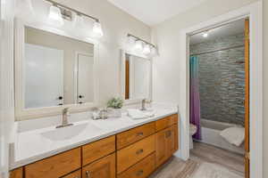 Bathroom featuring double vanity, toilet, shower / tub combo with curtain, and a sink