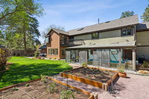 Rear view of property with a sunroom, a lawn, a garden, brick siding, and central AC unit