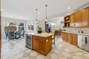 Kitchen featuring beverage cooler, light countertops, stainless steel dishwasher, a glass covered fireplace, and open shelves