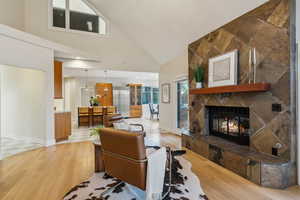 Living room with a stone fireplace, baseboards, light wood-type flooring, and a towering ceiling