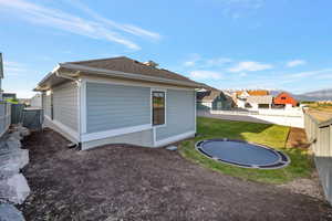 Rear view of property with a trampoline, a shingled roof, and a mountain view