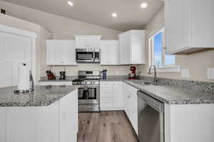 Kitchen with light wood-style flooring, a sink, vaulted ceiling, appliances with stainless steel finishes, and white cabinetry