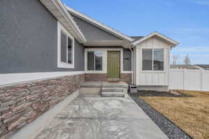 View of exterior entry with fence, board and batten siding, stone siding, and stucco siding