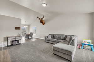 Carpeted living room with a notable chandelier, visible vents, baseboards, and lofted ceiling