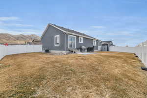 Back of property with central air condition unit, a lawn, a fenced backyard, a patio area, and a mountain view