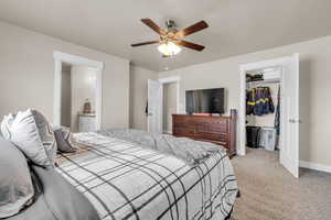 Bedroom with a walk in closet, a closet, baseboards, light colored carpet, and ceiling fan