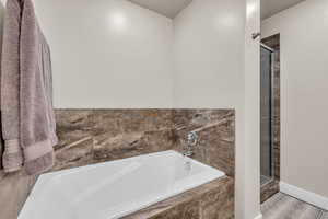 Full bathroom featuring a bath, baseboards, and a stall shower