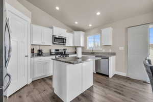 Kitchen with lofted ceiling, appliances with stainless steel finishes, wood finished floors, stone countertops, and white cabinetry