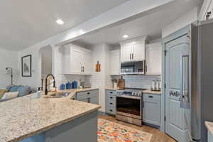 Kitchen featuring light stone countertops, light wood-style flooring, appliances with stainless steel finishes, white cabinets, and a sink