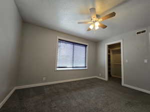 Master has a South window with plenty of light and a walk in closet, ceiling fan, and dark carpet