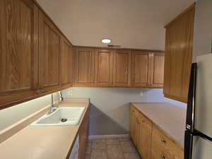 Kitchen featuring a sink, freestanding refrigerator, plenty of wood cabinetry, light countertops, and light tile patterned floors