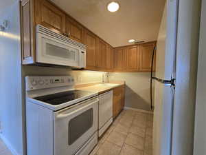 Kitchen featuring light tile patterned floors, brown cabinets, white appliances, and sink.