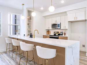 Kitchen featuring light wood-style floors, stainless steel appliances, baseboards, white cabinetry, and light stone countertops