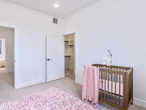 Carpeted bedroom with a spacious closet, visible vents, a crib, and baseboards