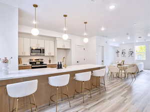 Kitchen featuring white cabinets, light wood-style floors, appliances with stainless steel finishes, and a breakfast bar