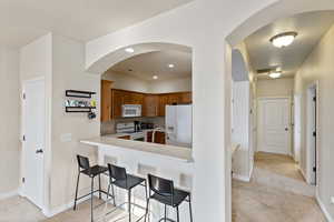Kitchen featuring a breakfast bar area, light countertops, light carpet, and white appliances