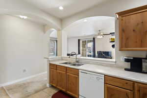 Kitchen featuring a ceiling fan, arched walkways, a sink, light countertops, and dishwasher
