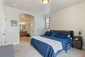 Bedroom with arched walkways, light carpet, ensuite bathroom, and electric panel