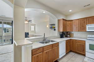 Kitchen featuring white appliances, a peninsula, a sink, and light countertops