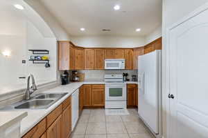 Kitchen with a sink, white appliances, light countertops, and light tile patterned floors