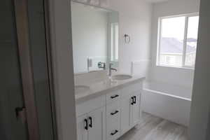 Full bathroom featuring double vanity, a garden tub, wood finished floors, and a sink