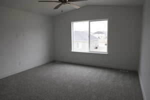 Carpeted empty room with lofted ceiling, baseboards, visible vents, and ceiling fan