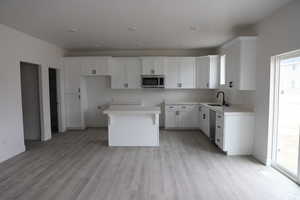 Kitchen featuring a kitchen island, light wood-style flooring, stainless steel appliances, and a sink