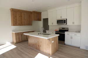 Kitchen featuring a center island with sink, light countertops, appliances with stainless steel finishes, light wood-style floors, and a sink