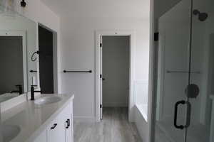 Full bath featuring double vanity, wood finished floors, a shower with shower door, and a sink