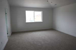 Empty room featuring visible vents, baseboards, light colored carpet, and lofted ceiling
