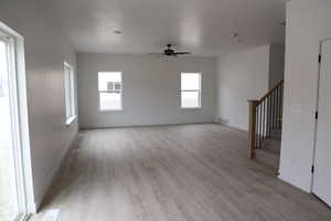 Unfurnished living room featuring stairs, visible vents, light wood-style floors, and a ceiling fan