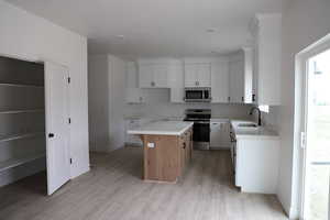 Kitchen with light wood-type flooring, a sink, a center island, white cabinetry, and appliances with stainless steel finishes