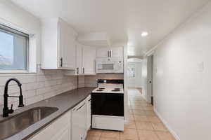 Kitchen featuring a sink, dark countertops, white appliances, arched walkways, and light tile patterned flooring
