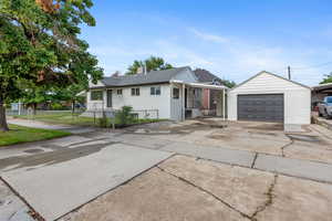 View of front facade with an outbuilding, driveway, a detached garage, fence, and a chimney
