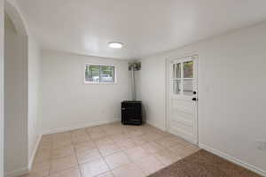 Empty room with light tile patterned floors, arched walkways, a wood stove, and baseboards