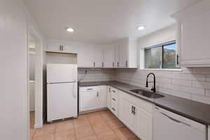 Kitchen featuring white appliances, light tile patterned flooring, a sink, white cabinets, and dark countertops