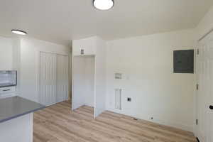 Laundry room with hookup for a washing machine, baseboards, light wood-style flooring, electric panel, and electric dryer hookup