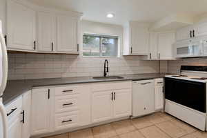 Kitchen featuring a sink, backsplash, dark countertops, white appliances, and white cabinets