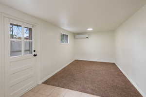 Interior space with an AC wall unit, light tile patterned floors, light colored carpet, and baseboards