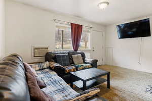 Living area with baseboards, carpet floors, and an AC wall unit