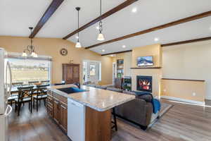 Kitchen with vaulted ceiling with beams, light countertops, a glass covered fireplace, white appliances, and a sink