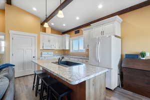 Kitchen with white appliances, light wood-style flooring, vaulted ceiling with beams, and a sink